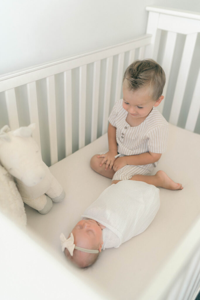 toddler with newborn in crib photographed by newborn photographer in utah